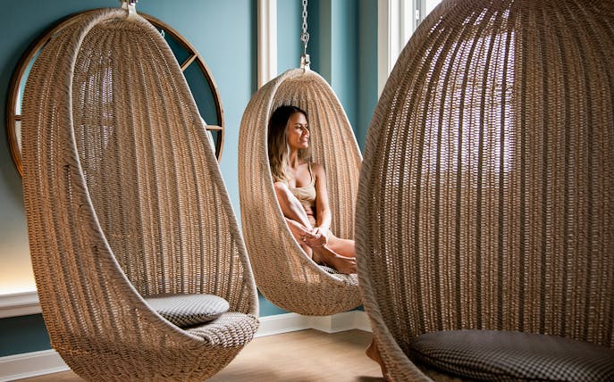 Person relaxing in a wicker hanging chair at QC New York spa.