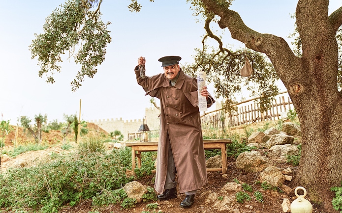 Performer in historical costume holding keys and a scroll at Puy du Fou España park.