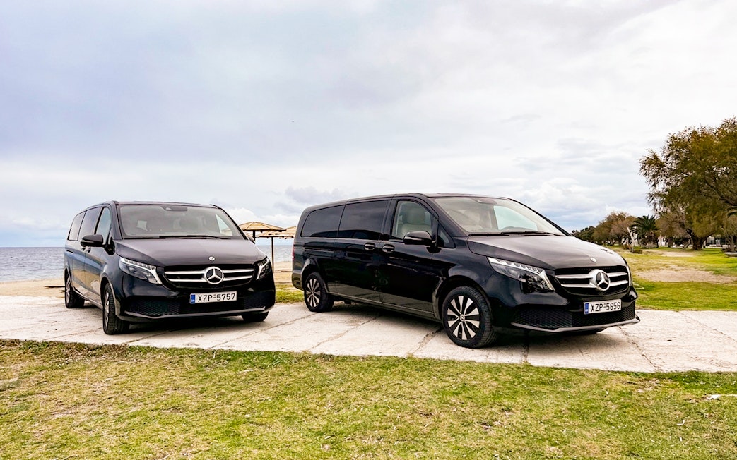 Two black Mercedes vans parked by the seaside, part of the Sensational Meteora Private Day Tour from Athens.