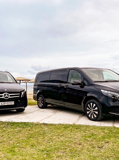 Two black Mercedes vans parked by the seaside, part of the Sensational Meteora Private Day Tour from Athens.