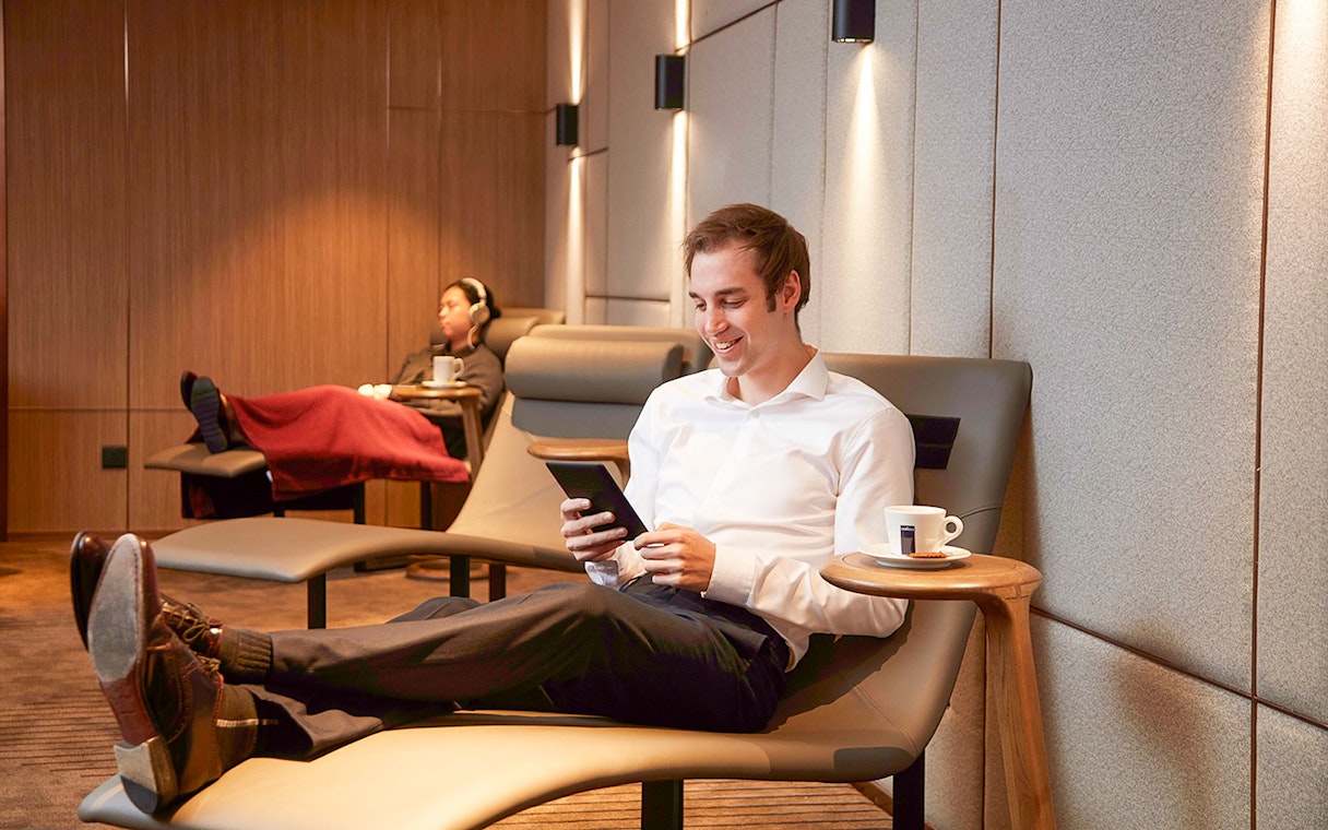Relaxing in first-class lounge at Hong Kong International Airport with coffee and tablet.