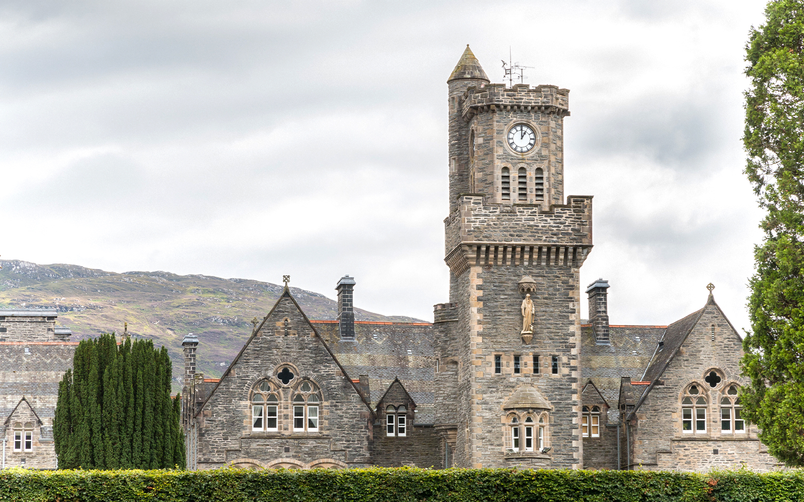Clock tower and stone building in Fort Augustus, Scotland, with hills in the background.