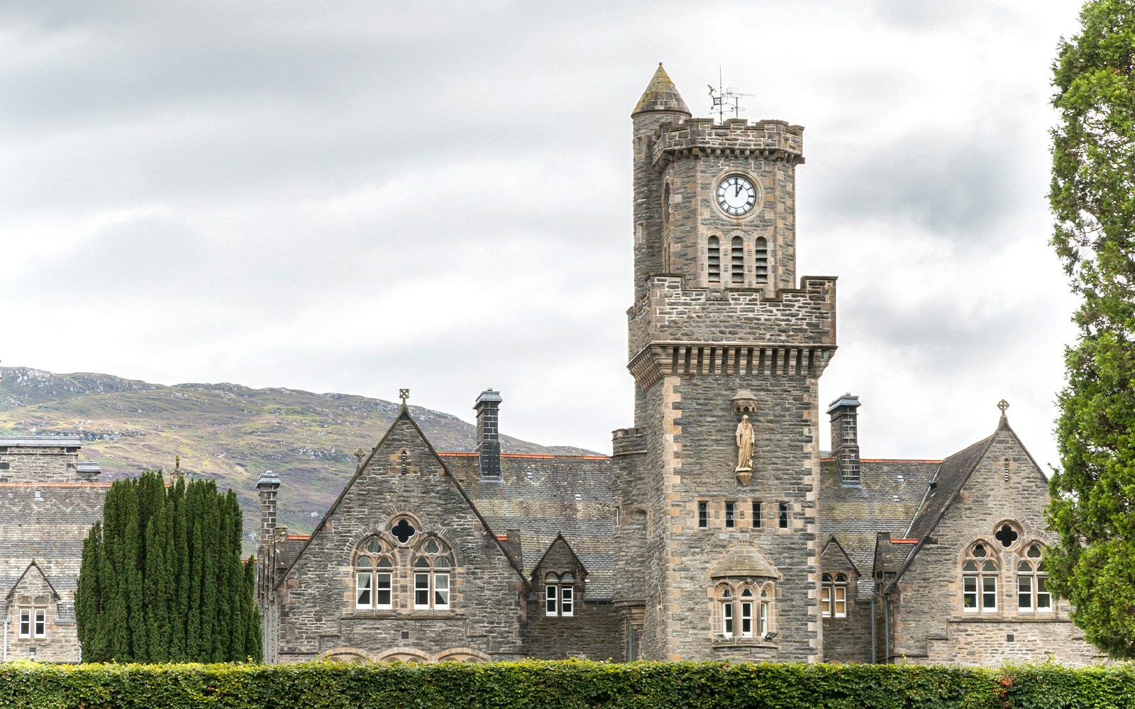 Clock tower and stone building in Fort Augustus, Scotland, with hills in the background.