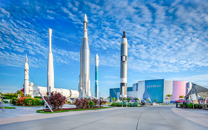 Kennedy Space Center facade with rockets on display under a blue sky.