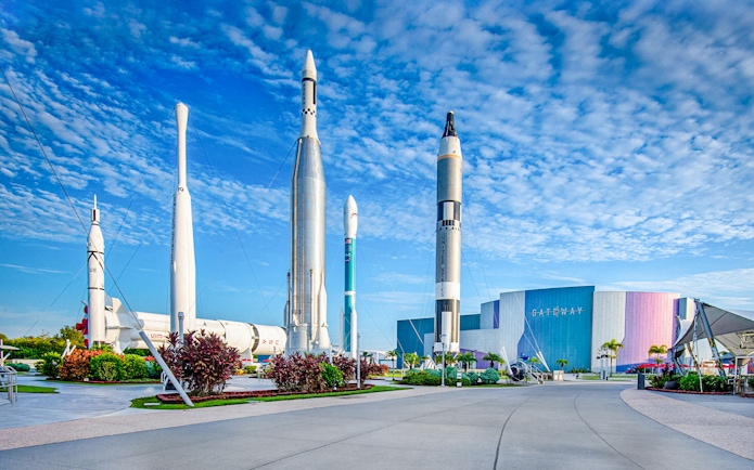 Kennedy Space Center facade with rockets on display under a blue sky.