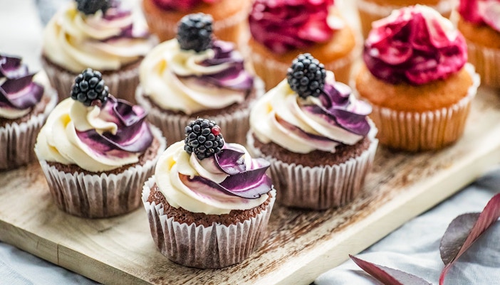Cupcakes with blackberry and cream frosting on a wooden tray.