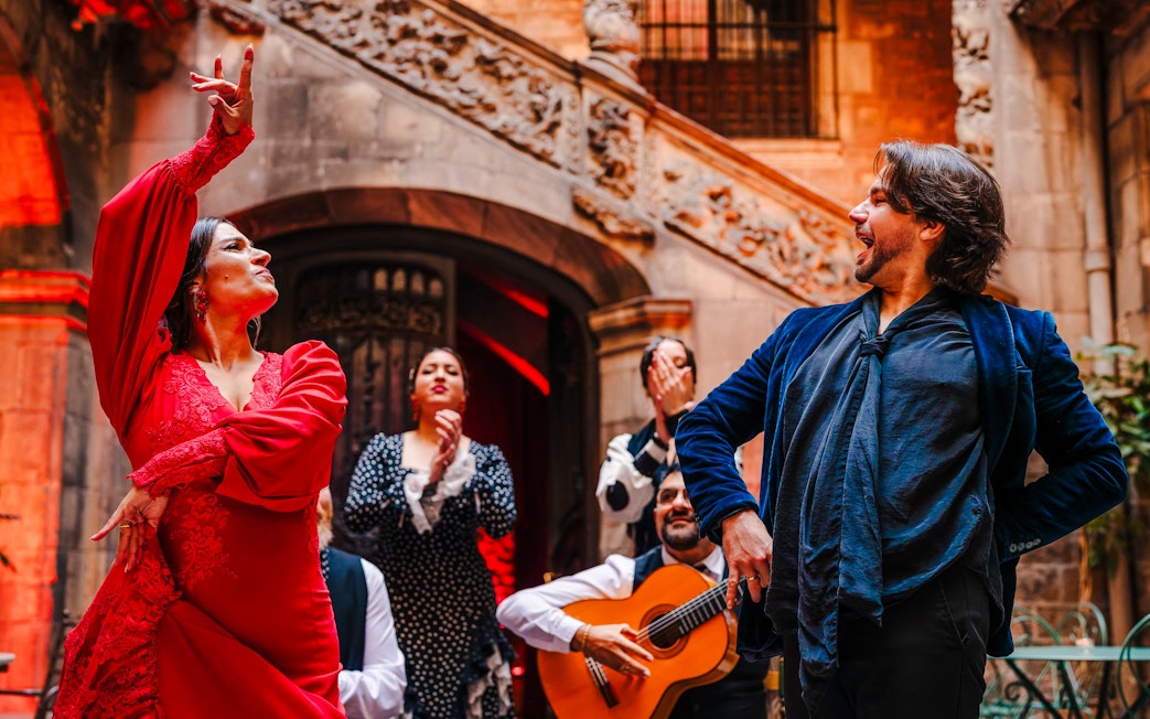 Flamenco dancers performing at Palau Dalmases with guitarist in background.