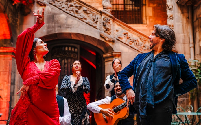 Flamenco dancers performing at Palau Dalmases with guitarist in background.