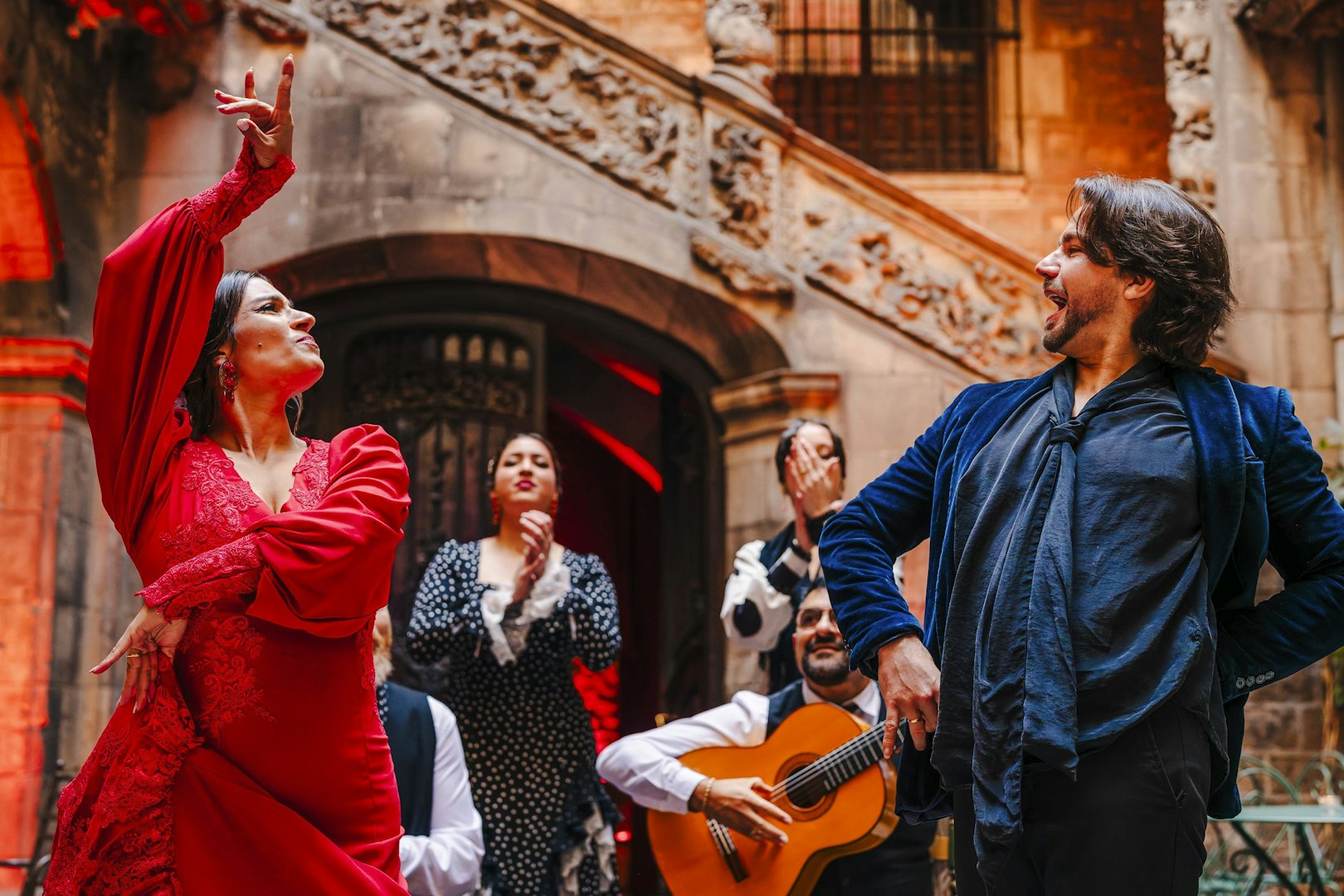 Flamenco dancers performing at Palau Dalmases with guitarist in background.