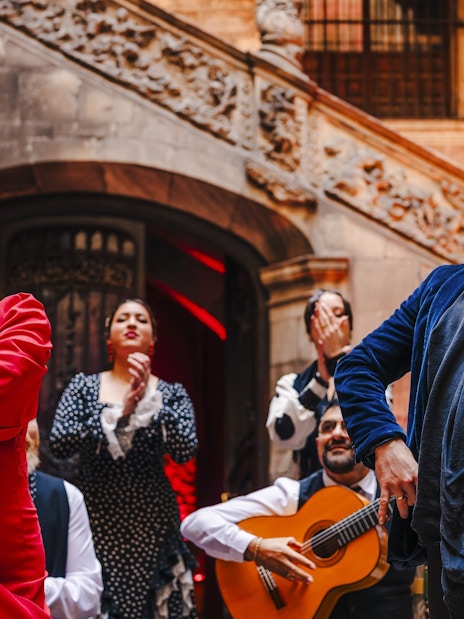 Flamenco dancers performing at Palau Dalmases with guitarist in background.