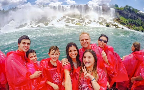 Tourists in red ponchos on a Niagara Falls cruise with the waterfall in the background.
