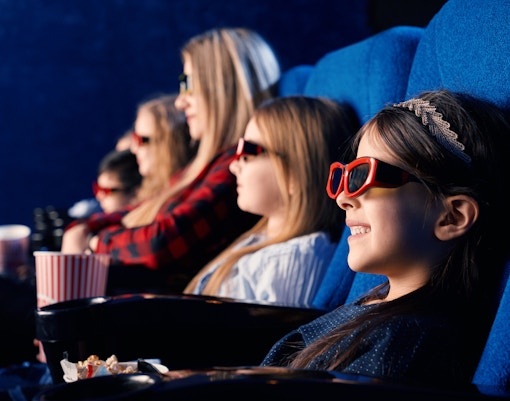 Young girl wearing 3D glasses at 4D cinema, smiling in theater seat.