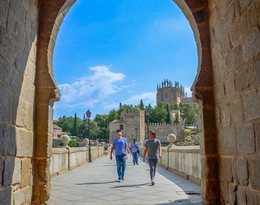 Visitors walking with a guide on San Martín Bridge, Toledo, with historic architecture in view.