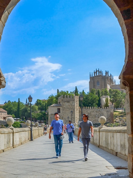 Visitors walking with a guide on San Martín Bridge, Toledo, with historic architecture in view.