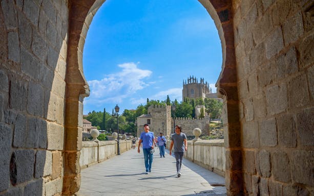 Visitors walking with a guide on San Martín Bridge, Toledo, with historic architecture in view.