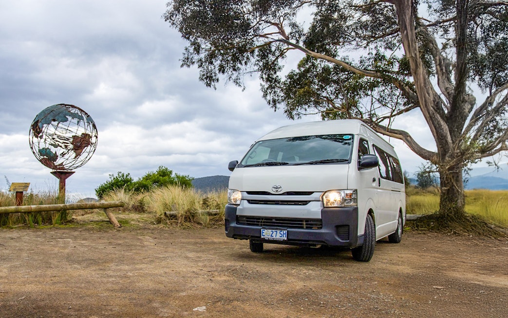 Tour van parked near a globe sculpture on Bruny Island, Tasmania.