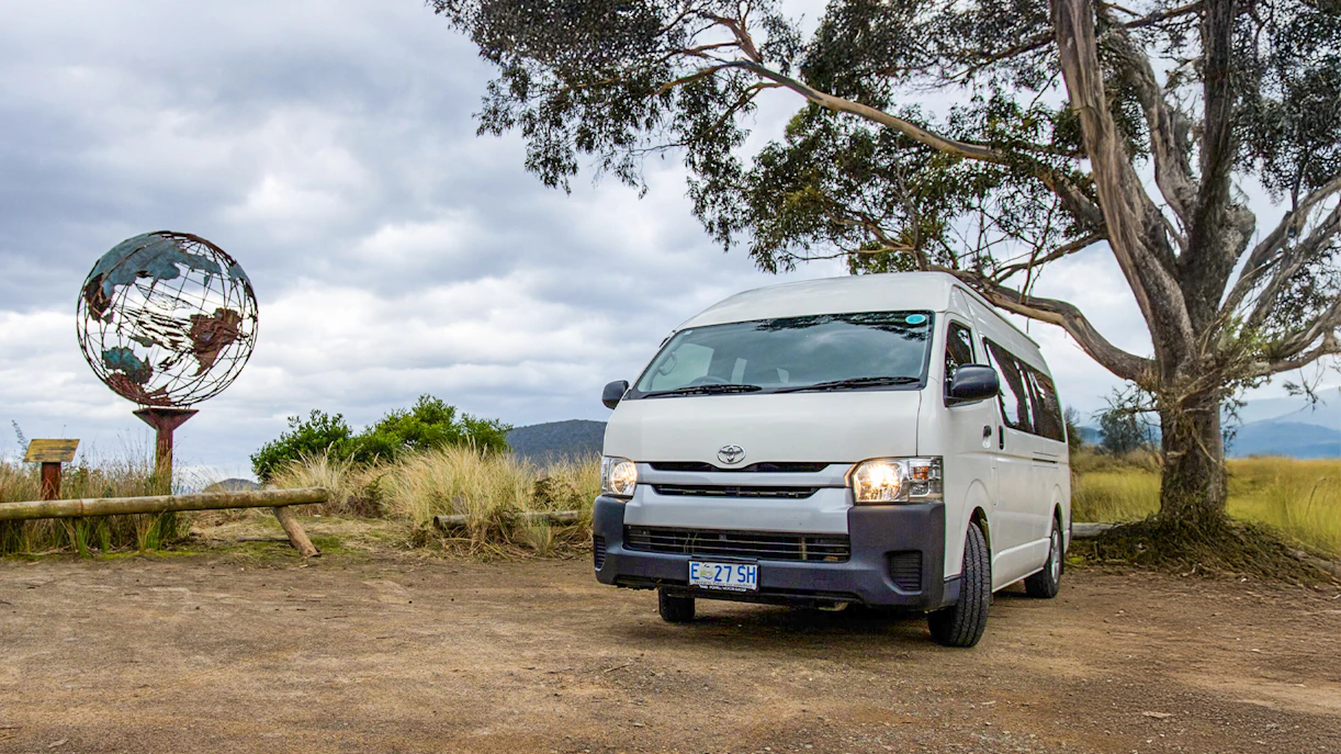 Tour van parked near a globe sculpture on Bruny Island, Tasmania.