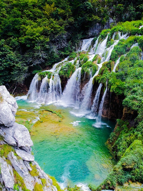 Waterfall cascading over lush greenery in Plitvice Lakes National Park, Croatia.