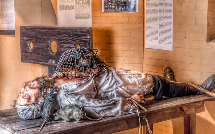 Medieval Torture Museum exhibit with a figure on a table, rats, and a cage.