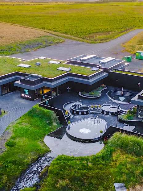 Krauma Geothermal Baths complex surrounded by green landscape in Iceland.