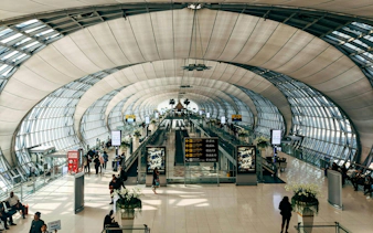 Interior view of Suvarnabhumi Airport terminal with travelers and moving walkways.