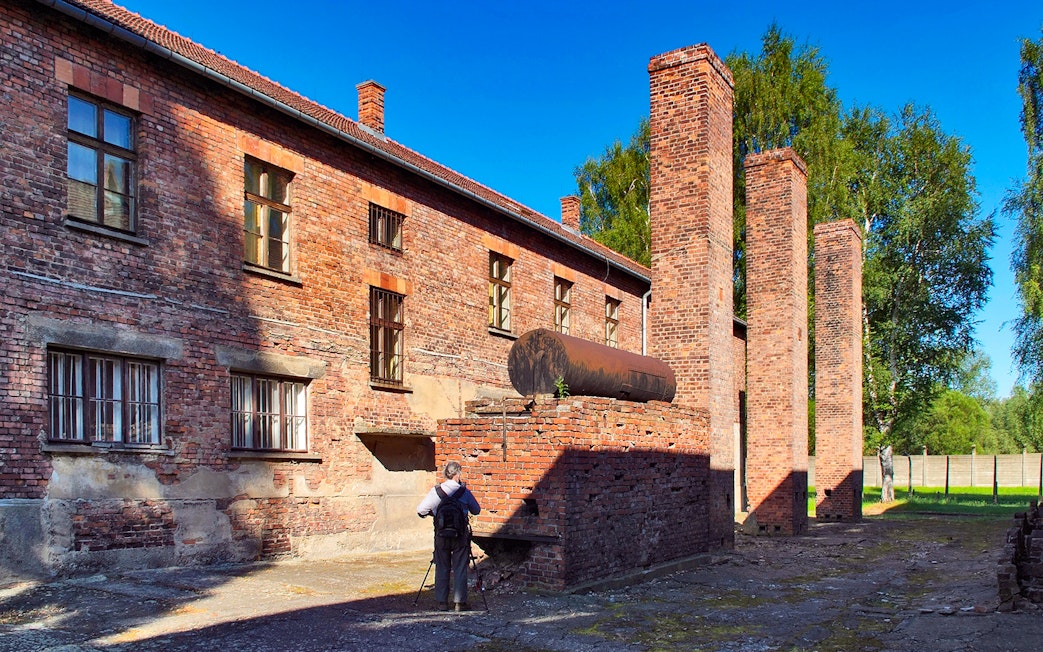Barrack building and chimneys at Auschwitz Birkenau, Poland, with a visitor taking photos.