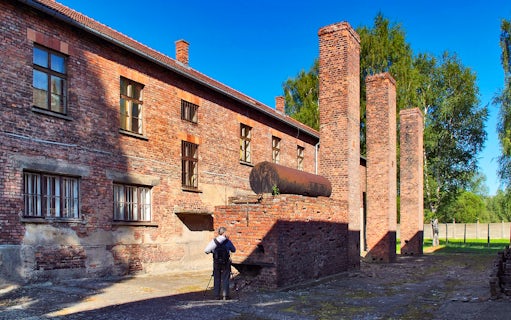 Barrack building and chimneys at Auschwitz Birkenau, Poland, with a visitor taking photos.