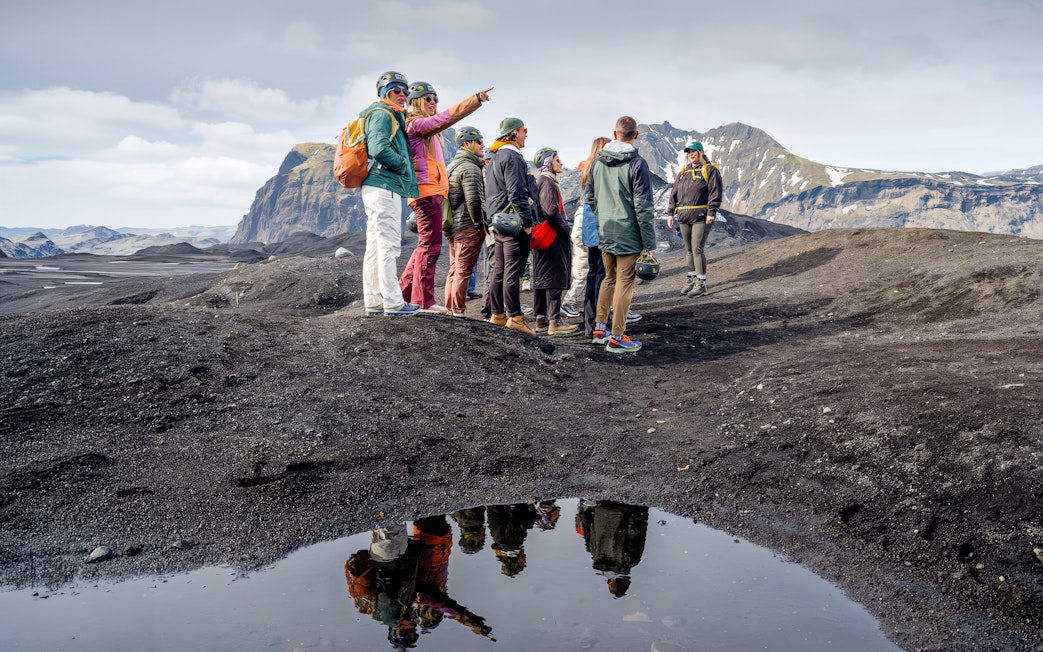 Group hiking on Sólheimajökull glacier, Iceland, with mountainous backdrop.