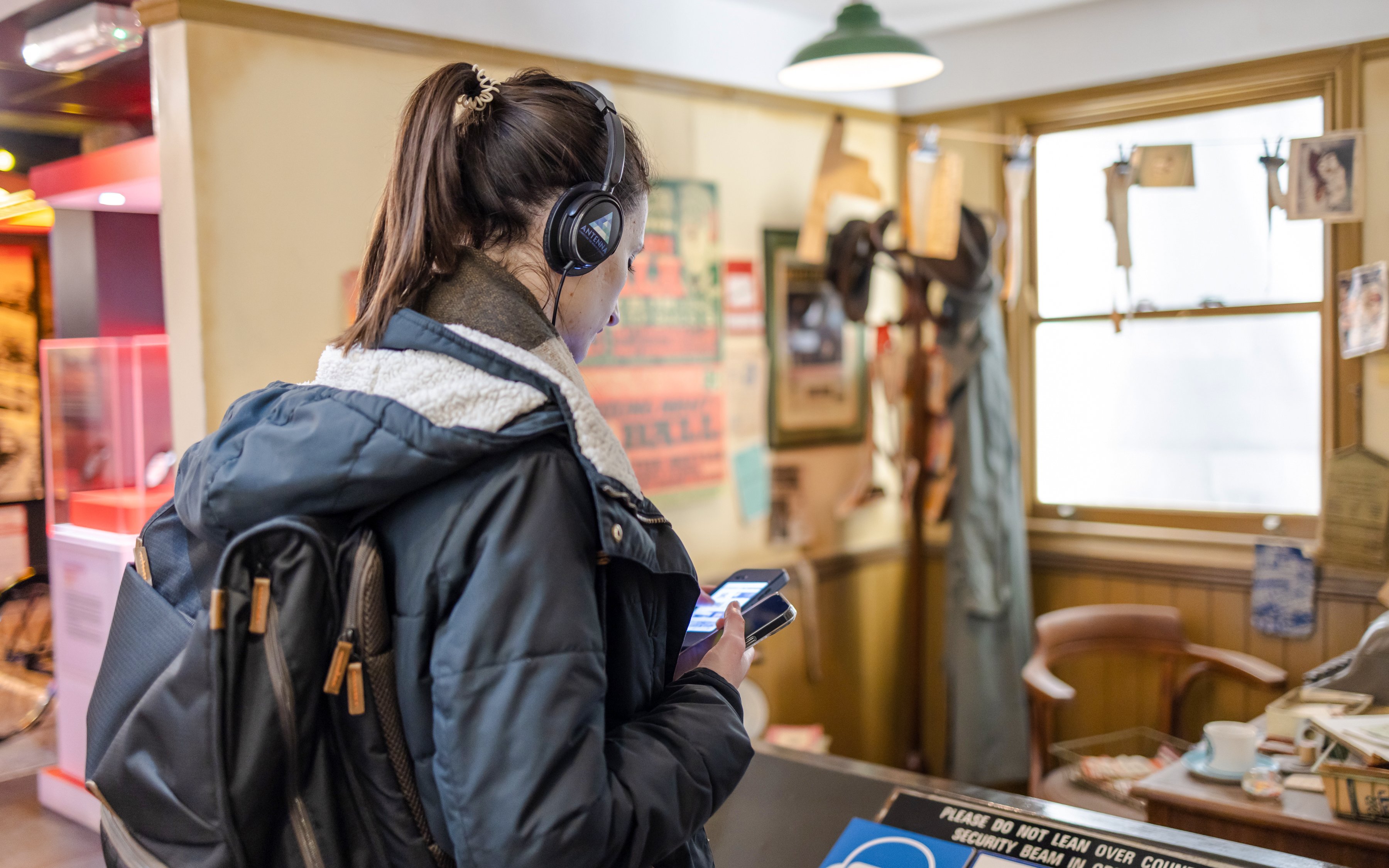 Visitor exploring The Beatles Story exhibit with headphones and smartphone.