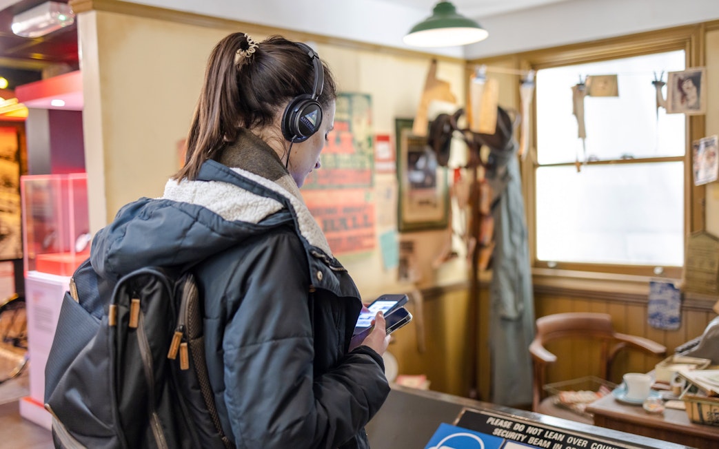 Visitor exploring The Beatles Story exhibit with headphones and smartphone.