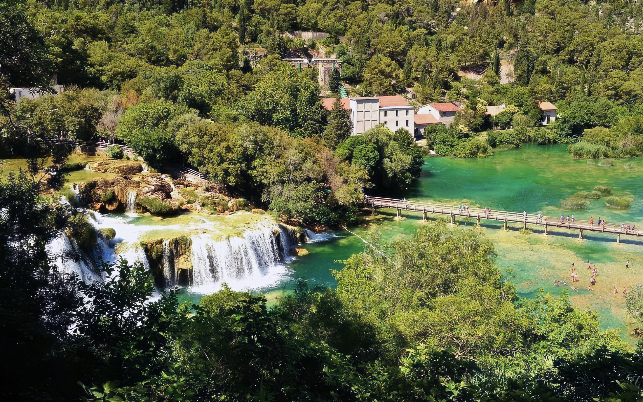 Waterfalls and footbridge at Krka National Park, Croatia, surrounded by lush greenery.