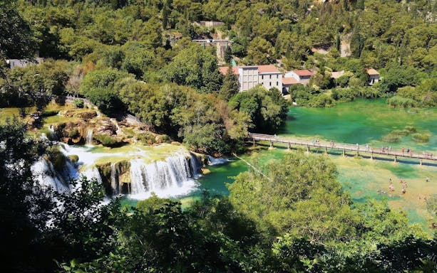 Waterfalls and footbridge at Krka National Park, Croatia, surrounded by lush greenery.