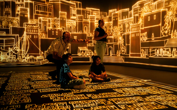 Visitors at London Timewalk Exhibition viewing illuminated historical cityscape.