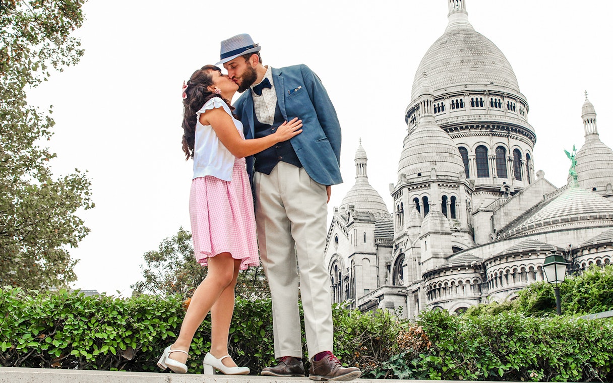 Couple kissing in front of Sacré-Cœur Basilica during Montmartre photoshoot experience.