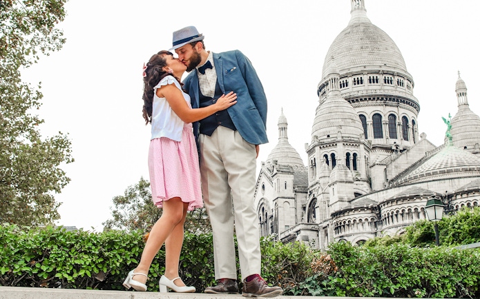Couple kissing in front of Sacré-Cœur Basilica during Montmartre photoshoot experience.