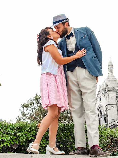 Couple kissing in front of Sacré-Cœur Basilica during Montmartre photoshoot experience.
