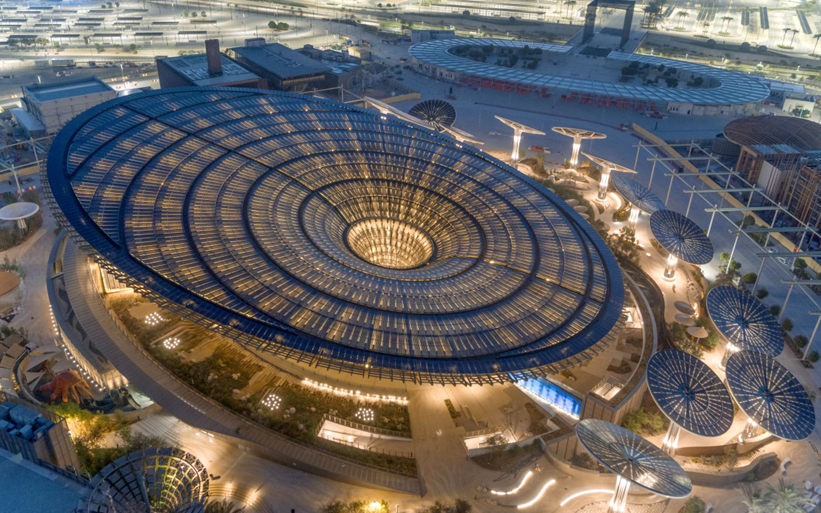 Aerial view of Expo City Dubai's illuminated Sustainability Pavilion at night.
