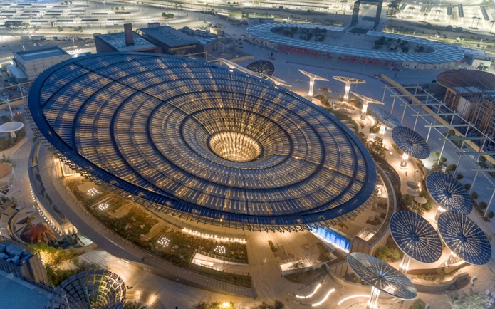 Aerial view of Expo City Dubai's illuminated Sustainability Pavilion at night.