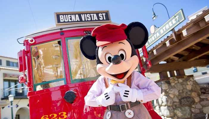 Mickey Mouse in front of the Buena Vista Street train ride at Disneyland Park, California.