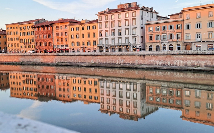 Colorful buildings along the Arno River in Pisa, Italy, reflecting in the water.