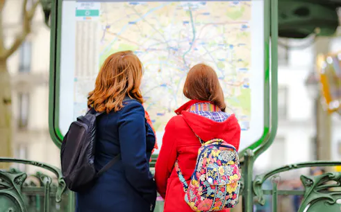 Two people with backpacks looking at a map in Le Marais, Paris.