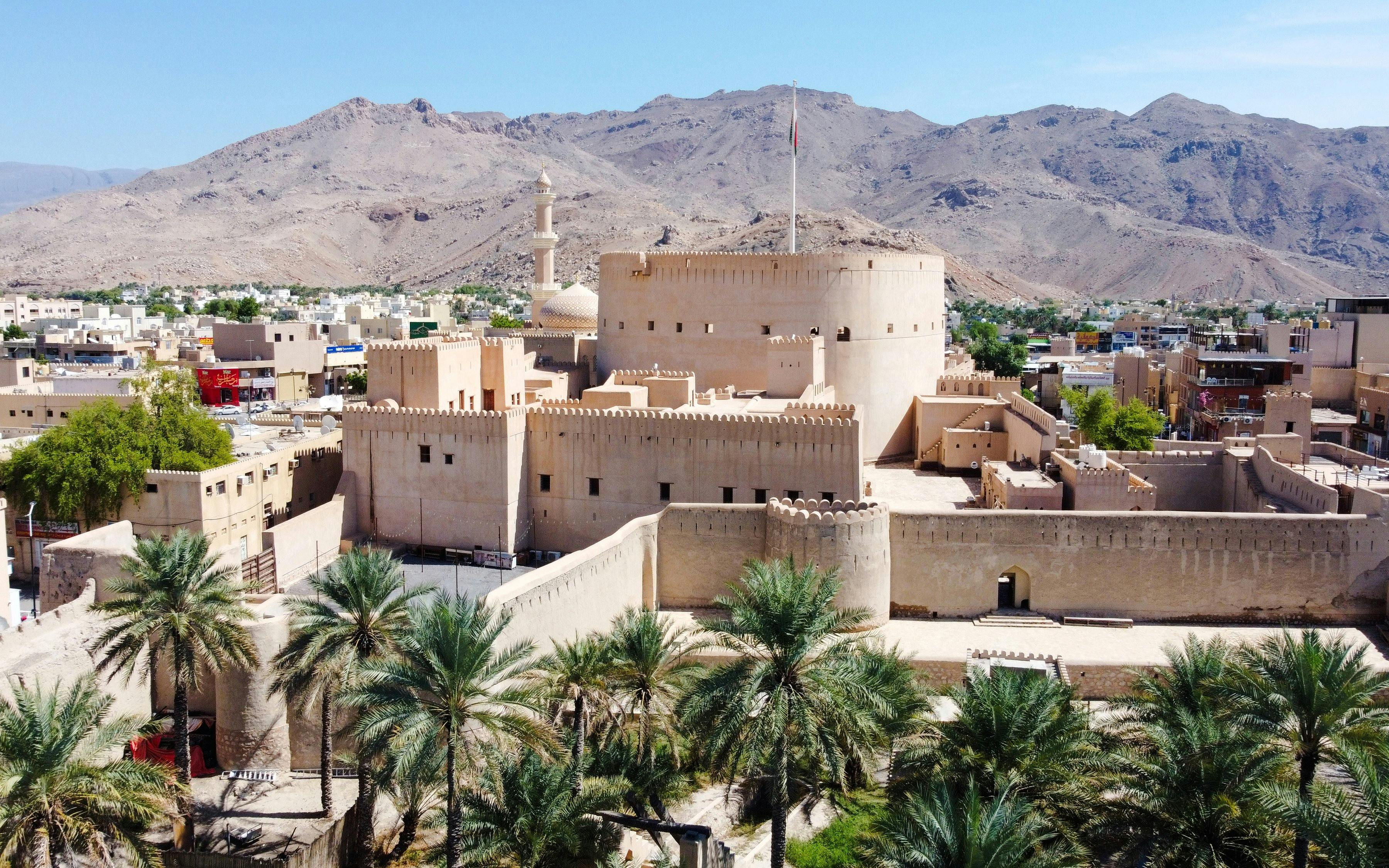 Aerial view of Nizwa Fort in Oman with surrounding mountains and palm trees.