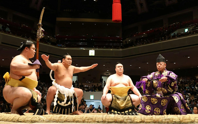 Sumo wrestlers and referee in traditional attire at Nagoya Sumo Tournament.