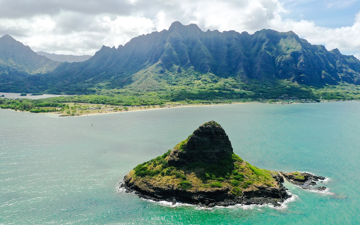 Aerial view of Mokoli'i Island near Kualoa Ranch, Hawaii with lush mountains in the background.