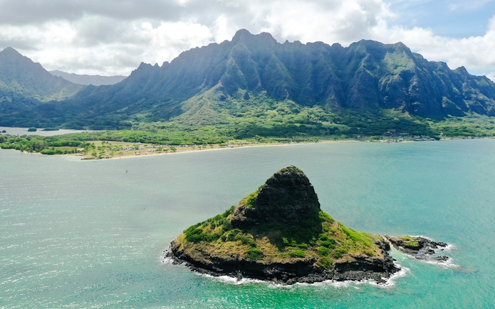 Aerial view of Mokoli'i Island near Kualoa Ranch, Hawaii with lush mountains in the background.
