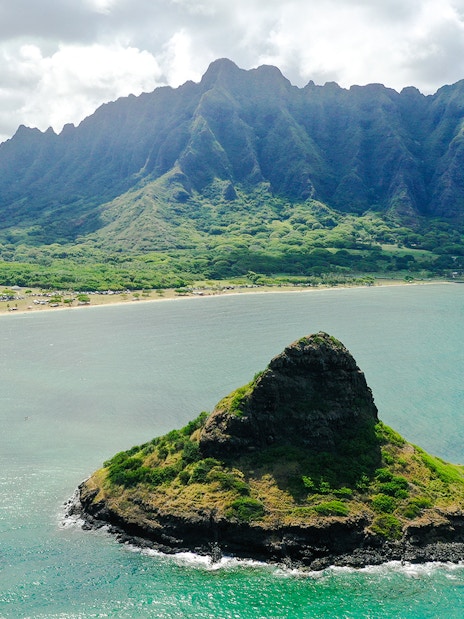 Aerial view of Mokoli'i Island near Kualoa Ranch, Hawaii with lush mountains in the background.