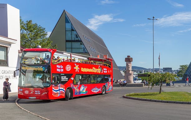 Oslo hop-on hop-off bus near modern architecture and sculpture.