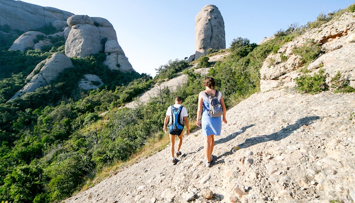 Woman hiking on Montserrat mountain trail, Spain, with scenic rocky landscape.