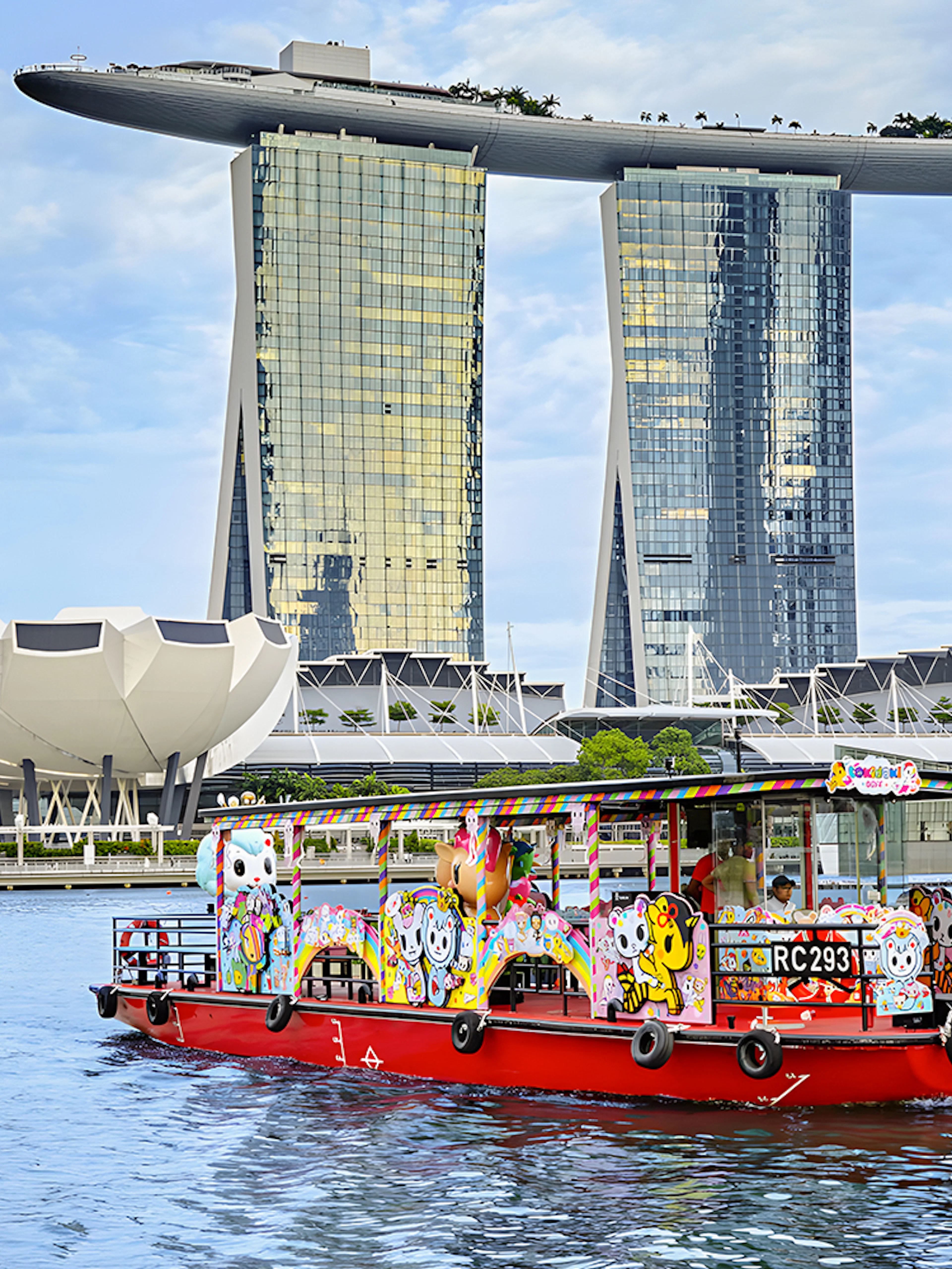 Singapore River Cruise boat with colorful designs in front of Marina Bay Sands.