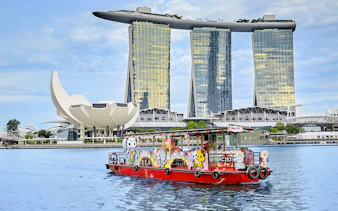Singapore River Cruise boat with colorful designs in front of Marina Bay Sands.